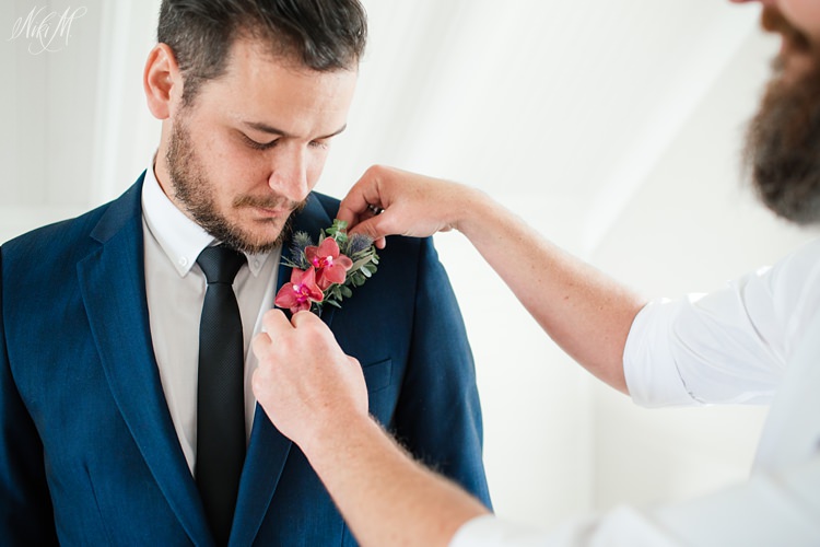 A groomsman pins on the groom's burgundy orchid boutonniere