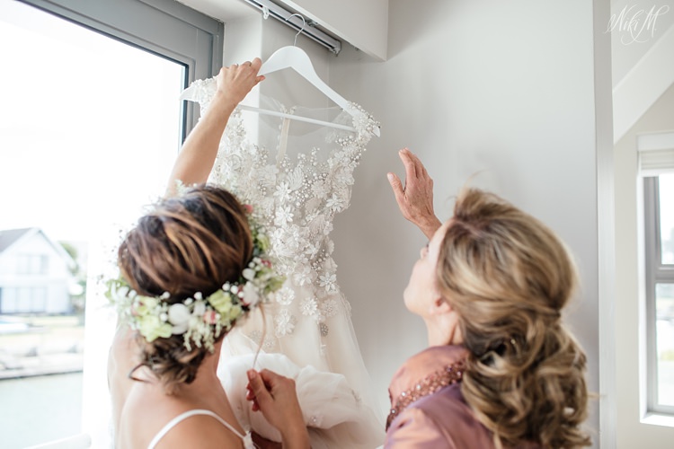 Bride and her mother lower the wedding gown which is decorated with laser cut details