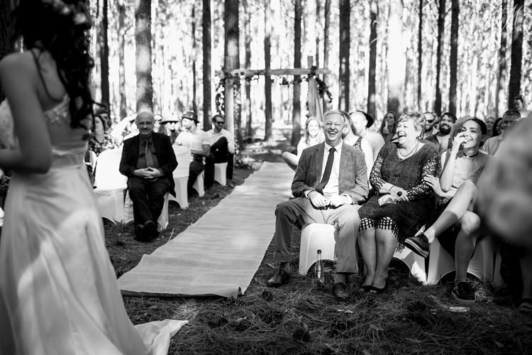 Sunlight filters through the forest trees onto the faces of laughing wedding guests