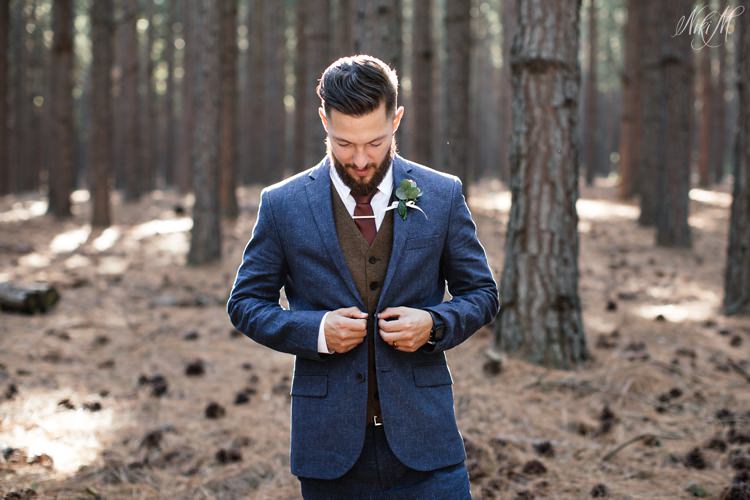 Groom Silvino adjusts his suit jacket surrounded by pine trees