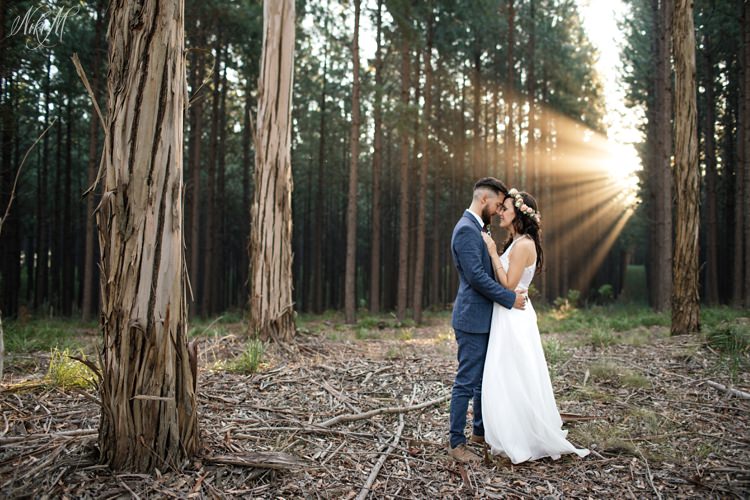 As the sun sets, the forest is filled with rays of light which fall on the newlywed couple