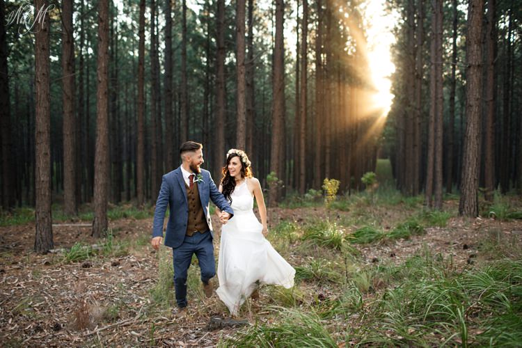 Amy and Silvino run through the forest filled with sun rays on their wedding day 